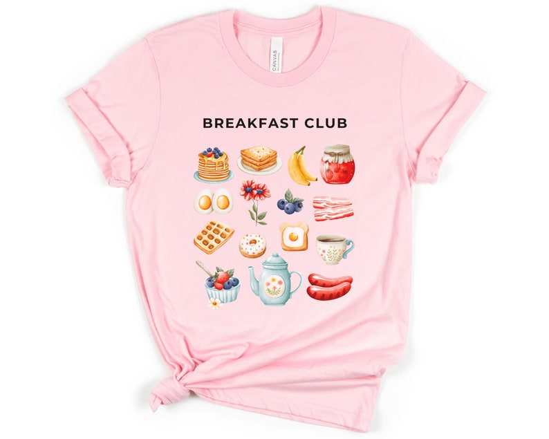 May include: Pink t-shirt with the text "Breakfast Club" and a graphic of various breakfast foods, including pancakes, eggs, bacon, waffles, donuts, coffee, and fruit.