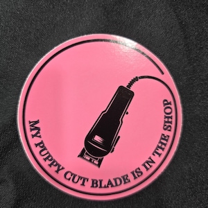 以下が含まれることがあります： 電気バリカンと「My Puppy Cut Blade Is In The Shop」というテキストが書かれたピンクの丸いステッカーです。