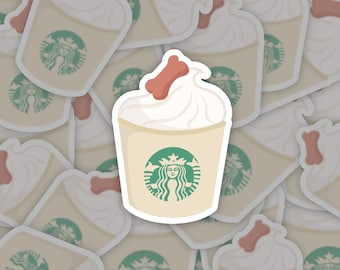 May include: A white coffee cup with a green Starbucks logo and a pink bone on top of the whipped cream. The cup is surrounded by other similar cups.