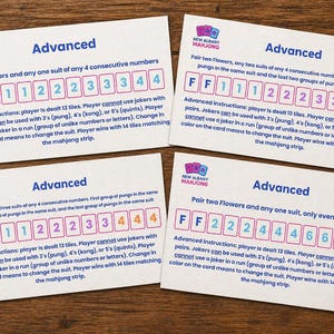 May include: Four white Mahjong game cards with the word "Advanced" at the top. Each card has a different combination of numbers and letters. The cards are on a wooden surface.