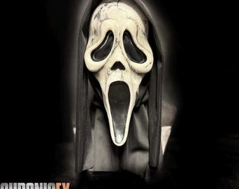 May include: A white, weathered-looking ghost mask with black mesh eye coverings and a long, open black mouth. The mask features dark, crack-like markings across the surface and is attached to a black fabric hood that drapes down the sides.