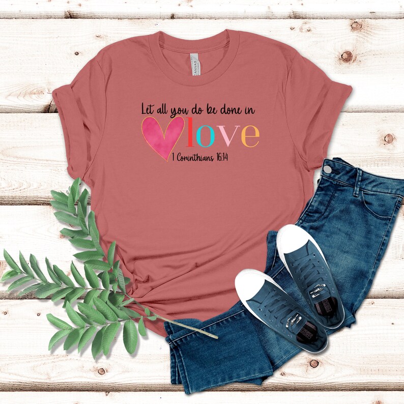 May include: A pink t-shirt with the text "Let all you do be done in love 1 Corinthians 16:14" in colorful letters with a pink heart.