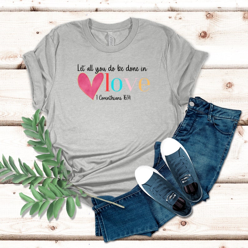 May include: A gray t-shirt with the text "Let all you do be done in love" and a pink heart with the words "love" in colorful letters. The text "1 Corinthians 16:14" is below the heart.