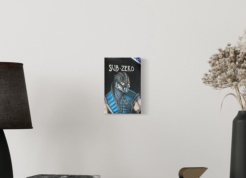 May include: A black and white drawing of Sub-Zero, a character from the Mortal Kombat video game series. The drawing is on a black background with the text "SUB-ZERO" in white.