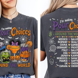 May include: A charcoal grey t-shirt featuring a graphic print with the text "I'm making Pour Choices AROUND THE WORLD". The design includes illustrations of cocktails, pumpkins, spiderwebs, and a list of countries with corresponding toasts and mouse icons.
