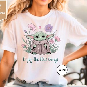 a woman wearing a white t - shirt with a picture of a baby yoda