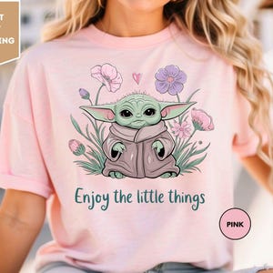 a woman wearing a pink t - shirt with a picture of a baby yoda