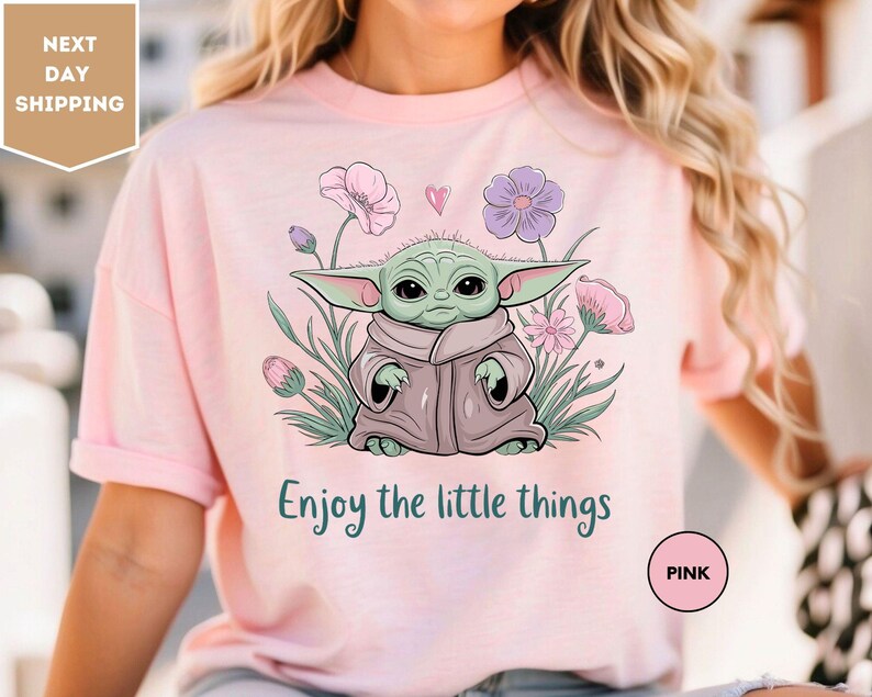 a woman wearing a pink t - shirt with a picture of a baby yoda