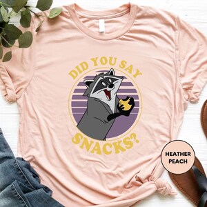 a pink shirt with a raccoon saying did you say snacks?