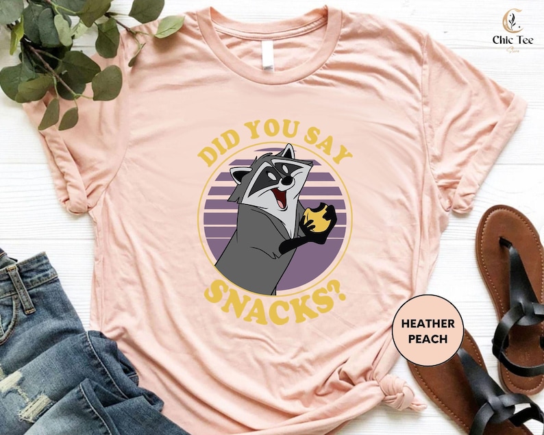 a pink shirt with a raccoon saying did you say snacks?