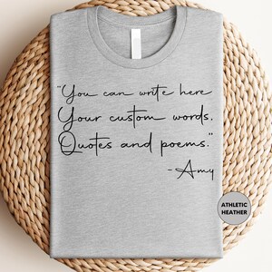 A gray t-shirt with a quote printed on it, placed on a woven mat.