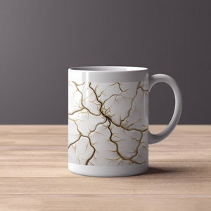 Może przedstawiać: Biały kubek ceramiczny z wzorem złotego pęknięcia. Kubek ma zaokrąglony uchwyt.