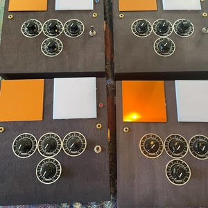 May include: Four dark wooden panels with various electronic components. Each panel has black knobs with white markings, orange and white squares, and small switches. The panels are arranged side by side.