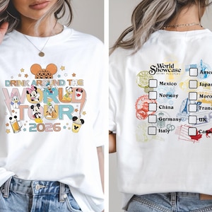 May include: White t-shirt featuring a colorful graphic of Disney characters and the text "DRINK AROUND THE WORLD TOUR 2026" on the front. The back of the shirt has a checklist of countries and the words "World Showcase Drink Passport".