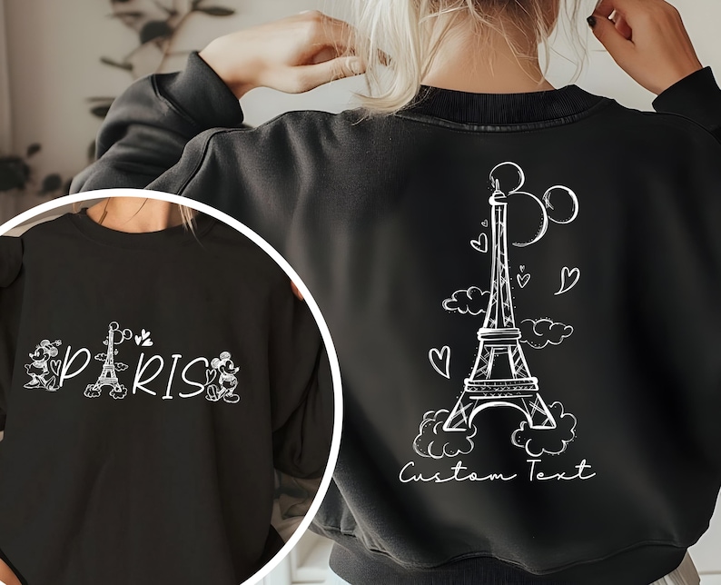 May include: Black sweatshirt with a white graphic of the Eiffel Tower, Mickey Mouse ears, and hearts. The text "Paris" and Mickey Mouse figures are on the front of the sweatshirt. The text "Custom Text" is on the back of the sweatshirt.
