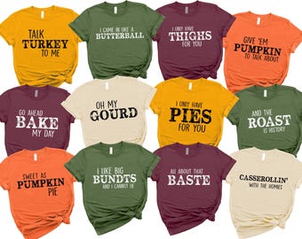 May include: A collection of colorful t-shirts with various Thanksgiving-themed phrases in bold white text. The shirts come in shades of orange, yellow, green, burgundy, and cream. Phrases include "Talk Turkey to Me" and "Oh My Gourd."