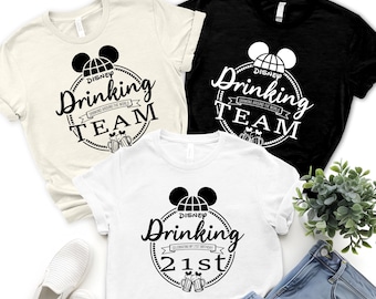 May include: Three t-shirts in cream, black, and white, each featuring a black graphic. The graphic includes a Mickey Mouse head, the words "Drinking Team" and "Drinking Around the World" in a circular design. One shirt says "Celebrating my 21st Birthday".