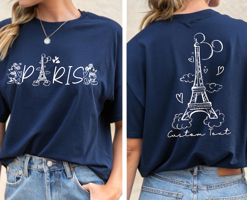 May include: A navy blue t-shirt with a white graphic of Mickey Mouse and Minnie Mouse in front of the Eiffel Tower with the word "PARIS" printed below. The back of the shirt has a white graphic of the Eiffel Tower with clouds and hearts and the text "Custom Text".
