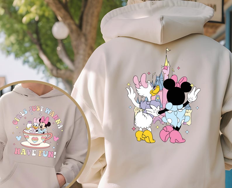 May include: A light beige hoodie with a graphic print of two Disney characters, Minnie Mouse and Daisy Duck, in front of Cinderella's Castle. The text "Girls Just Wanna Have Fun!" is printed on the front of the hoodie.