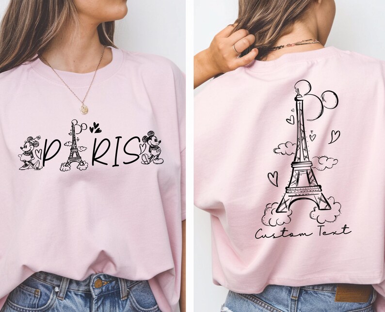 May include: Pink t-shirt with a black and white graphic of Mickey Mouse and Minnie Mouse in front of the Eiffel Tower with the word "PARIS" printed below. The back of the shirt has a black and white graphic of the Eiffel Tower with clouds and hearts. The text "Custom Text" is printed below the Eiffel Tower.