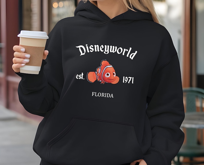 Puede incluir: Sudadera con capucha negra con un gr&aacute;fico blanco de un pez payaso y el texto "Disneyworld est. 1971 Florida".
