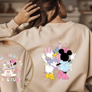 May include: A light beige sweatshirt with a graphic print of Minnie Mouse and Daisy Duck in front of a pink castle. The text "Girls Just Wanna Have Fun!" is printed on the front of the sweatshirt.