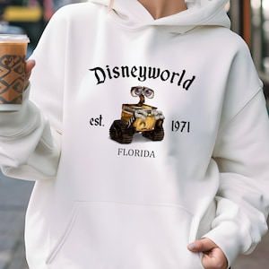 Puede incluir: Sudadera blanca con un gr&aacute;fico negro de un personaje robot de la pel&iacute;cula Wall-E. El gr&aacute;fico incluye el texto "Disneyworld est. 1971 Florida".