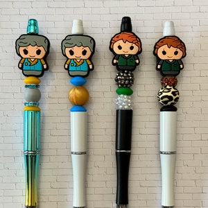 May include: Four pens with different colored beads and toppers. The toppers are cartoon characters with different colored hair and clothing. The pens are labeled A, B, C, and D.