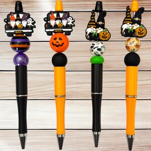 May include: Four Halloween-themed pens with decorative tops. The pens feature black and orange barrels, and various toppers including gnomes, pumpkins, and the word "BOO". The pens are designed for Halloween or seasonal use.