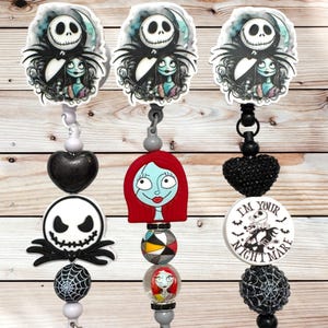 May include: Three badge reels featuring characters from The Nightmare Before Christmas. Each reel has a different design, including Jack Skellington and Sally, with decorative beads and charms. The background is a light wood grain.