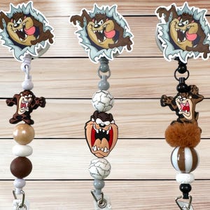 May include: Three retractable badge holders featuring the Tasmanian Devil cartoon character. Each holder has a different design, including a cartoon image of the character, and decorative beads in various colors.