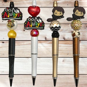 May include: Four decorative pens with unique designs. One pen has a black barrel with a gold sphere and a black topper. Another has a white barrel with a red heart topper. The third has a gold barrel with a Harry Potter character topper. The fourth has a brown barrel with a sparkly topper.