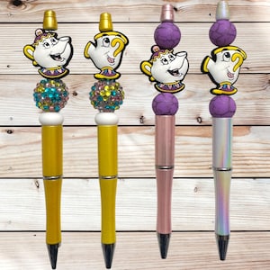 May include: Four decorative pens with cartoon teapot toppers. Two pens have yellow barrels, jewel-toned bead accents, and gold-colored tops. The other two pens have pink and iridescent barrels, purple bead accents, and silver-colored tops.