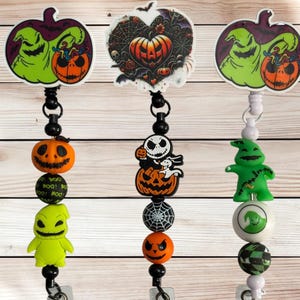 May include: Three Halloween-themed retractable badge holders. Each features a different design: a green character with a pumpkin, a heart-shaped design with a pumpkin, and a Jack Skellington character with a pumpkin. The holders have black beads and a silver clip.