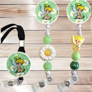 May include: Three retractable badge holders featuring a cartoon fairy design. Each holder has a round, green background with a fairy and daisies. The holders are adorned with green beads and a white daisy. One has a black lanyard.