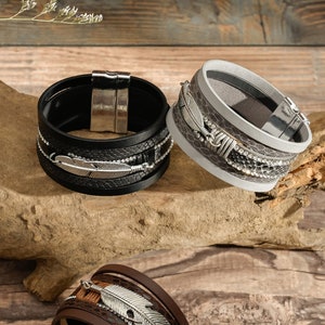 May include: Three leather bracelets with silver feather accents. The bracelets are in black, brown, and gray.