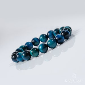 May include: A blue tiger's eye beaded bracelet. The beads are round and have a dark blue colour with a slight green hue.