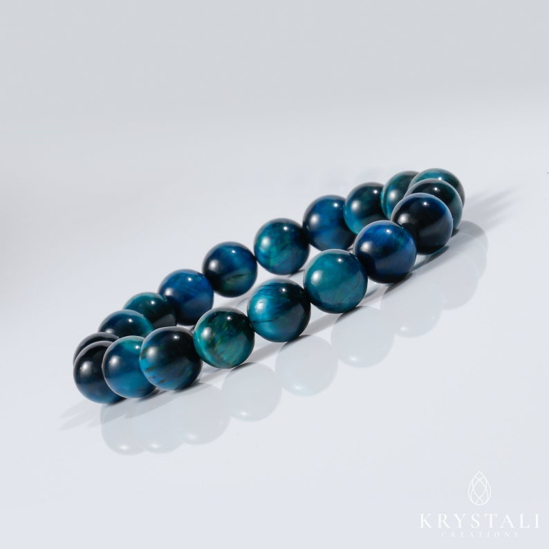 May include: A blue tiger's eye beaded bracelet. The beads are round and have a dark blue colour with a slight green hue.