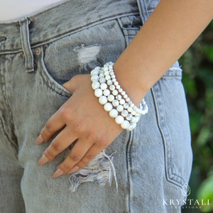 May include: A stack of five white howlite beaded bracelets. The bracelets are worn on a person's wrist.