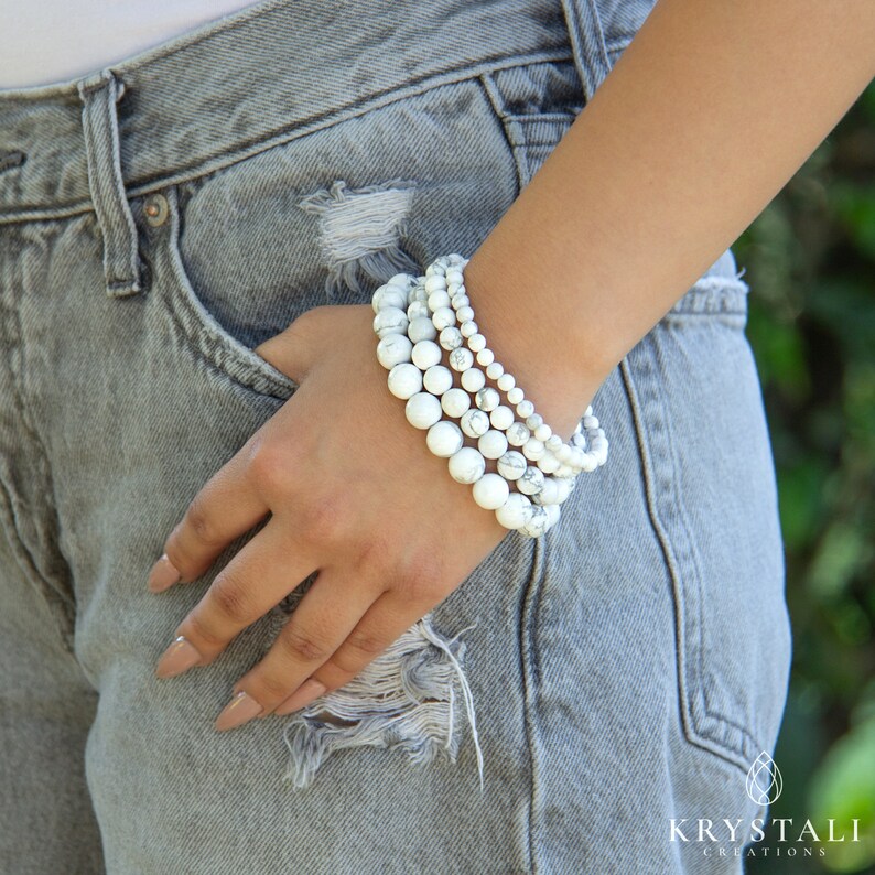 May include: A stack of five white howlite beaded bracelets. The bracelets are worn on a person's wrist.