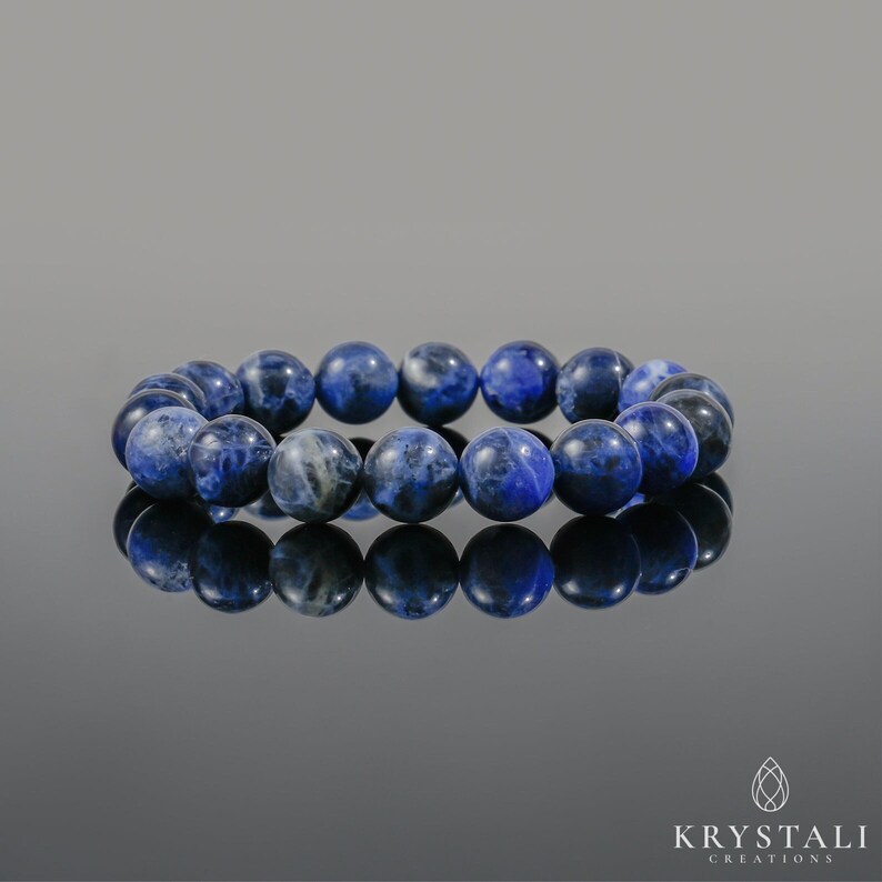Op de afbeelding: Een blauwe armband van ronde stenen kralen. De armband ligt op een reflecterend oppervlak.