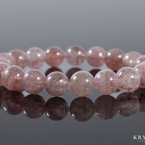 Op de afbeelding: Een armband gemaakt van roze en witte edelsteen kralen. De kralen zijn rond en hebben een gespikkeld uiterlijk.