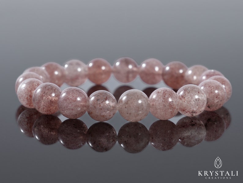 Op de afbeelding: Een armband gemaakt van roze en witte edelsteen kralen. De kralen zijn rond en hebben een gespikkeld uiterlijk.
