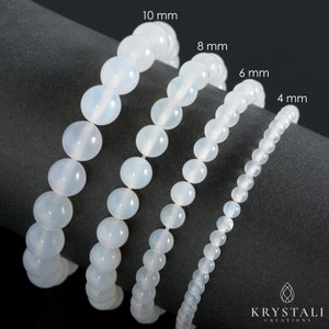 May include: Four white gemstone bracelets of different sizes, 4 mm, 6 mm, 8 mm, and 10 mm, laid out on a gray surface. The bracelets are made of round beads.