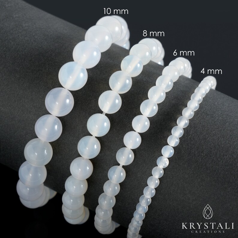 May include: Four white gemstone bracelets of different sizes, 4 mm, 6 mm, 8 mm, and 10 mm, laid out on a gray surface. The bracelets are made of round beads.