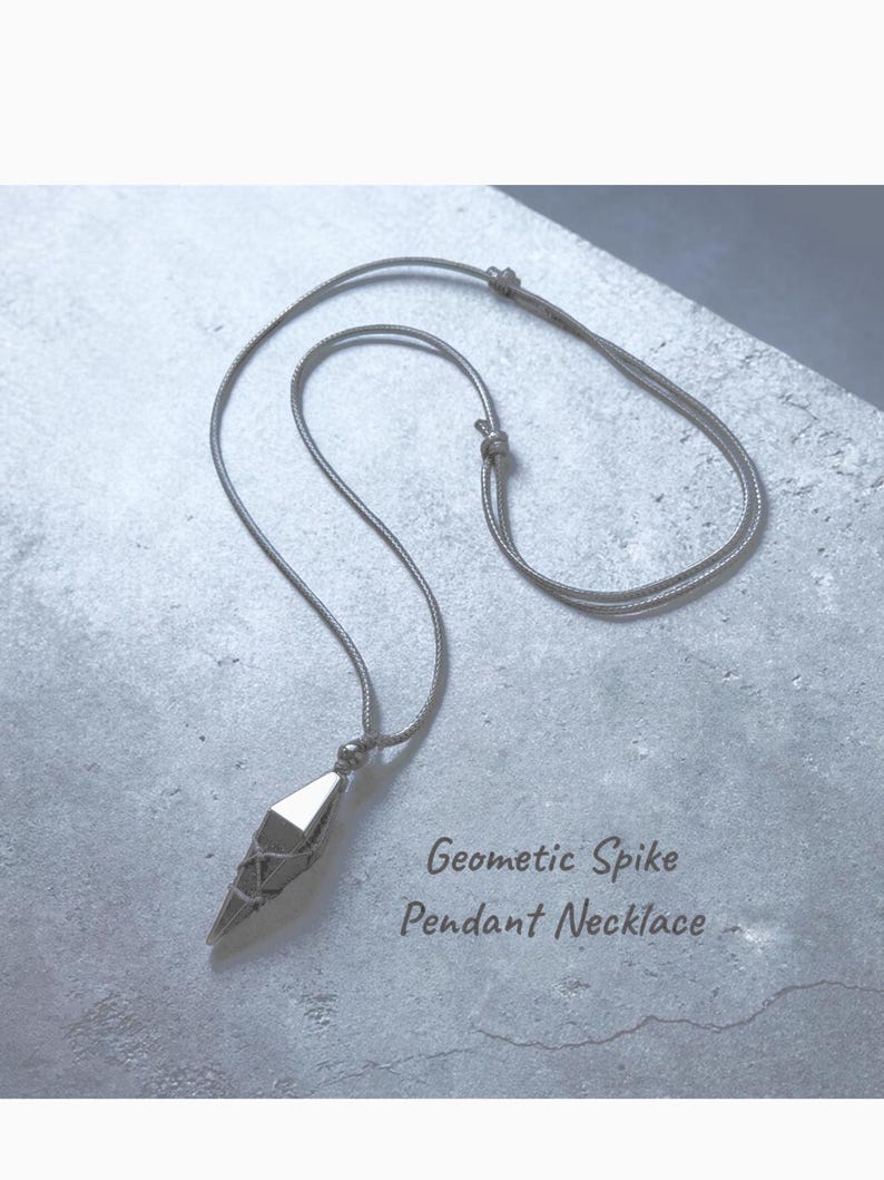 May include: A silver-toned geometric spike pendant necklace. The pendant has a faceted design and is suspended from a delicate chain. The text "Geometric Spike Pendant Necklace" is visible.