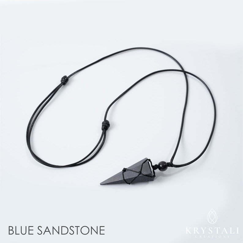 May include: A black necklace featuring a triangular blue sandstone pendant. The pendant is suspended from a black cord with adjustable knots. The words "BLUE SANDSTONE" are printed at the bottom of the image.