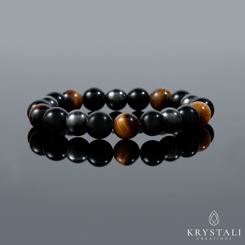 K&ouml;nnte beinhalten: Ein Armband mit schwarzen, braunen und goldenen Perlen. Das Armband besteht aus H&auml;matit-, Tigerauge- und Onyxsteinen.