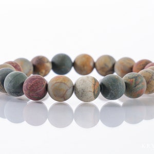 May include: A beaded bracelet featuring large, round beads in shades of green, brown, red, and tan. The beads have a matte finish and are strung together to form a circular shape. The bracelet is displayed on a white surface.