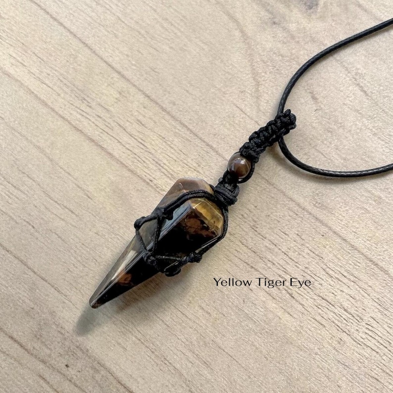 May include: A pendant necklace featuring a yellow tiger eye crystal. The crystal is encased in a black woven net and suspended from a black cord. The text "Yellow Tiger Eye" is visible on the image.